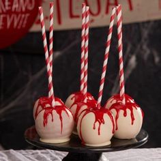 four white chocolate covered candy apples with red and white striped straws on a black plate