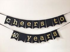 two black and gold cheers to 40 years banner hanging on a string with the words cheers to forty years