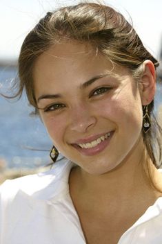 a young woman smiling at the camera with water in the background