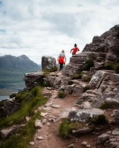 two people walking up the side of a rocky hill next to a body of water