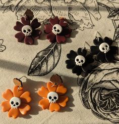 three pairs of skull and flower earrings on a tablecloth with flowers in the background