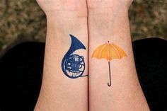 two people with matching tattoos on their arms holding an umbrella and a trumpet in front of them