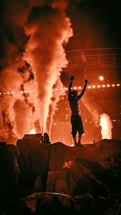 a man standing on top of a pile of rocks in front of a large fire