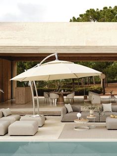 an outdoor living area with couches, tables and umbrellas by the swimming pool