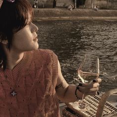 a woman sitting at a table with a glass of wine in her hand and looking out over the water