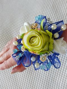 a woman's hand is holding a blue and green corsage with pearls