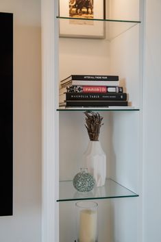 a glass shelf filled with books and a vase on top of it next to a candle