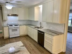 an empty kitchen with white cabinets and marble counter tops, wood floors, and a ceiling fan