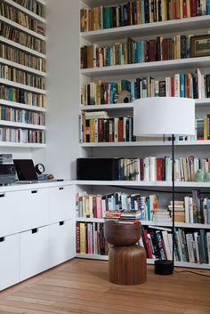 a room filled with lots of books next to a desk and lamp on top of a hard wood floor