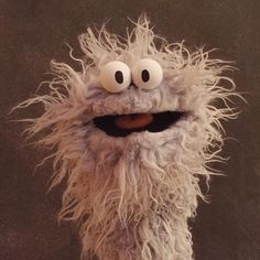 a close up of a stuffed animal with big eyes and long hair on a black background