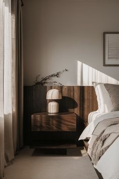 a bed sitting next to a window with curtains on either side and an end table in front of it