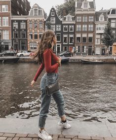 a woman is walking along the water in front of some buildings