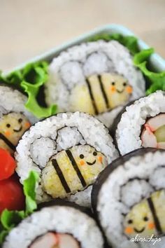 sushi rolls with smiley faces on them are in a plastic container filled with lettuce and tomatoes