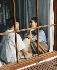 two people are sitting on the window sill looking at each other and laughing together