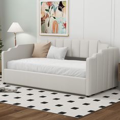 a white day bed sitting on top of a hard wood floor next to a lamp