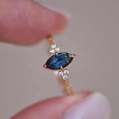 a woman's hand holding a ring with a blue stone and three diamonds on it