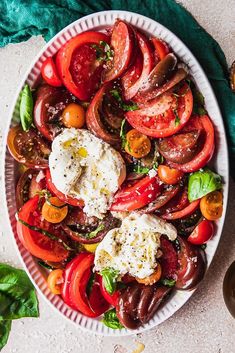 a white plate topped with tomatoes and mozzarella next to a bowl of olives