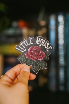 someone holding up a sticker that says little mouse with a red rose on it