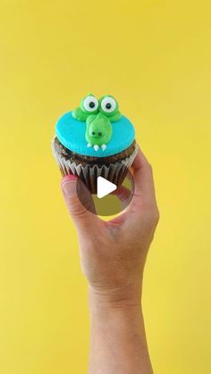 a person holding up a cupcake with googly eyes