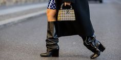 a woman walking down the street wearing black boots and a coat with an over - the - knee bag