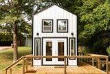 the tiny house is built on top of a wooden deck in front of some trees