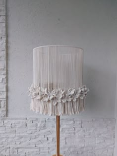 a white lamp on a wooden base with flowers and fringes hanging from it's side