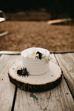 a small white cake sitting on top of a wooden table next to a tree slice