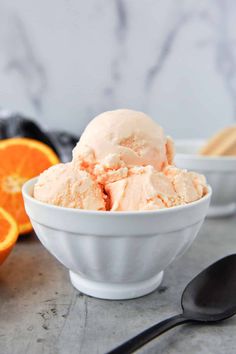 two bowls filled with orange ice cream next to an orange slice and spoon on a table