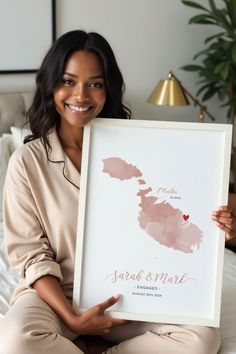 a woman sitting on a bed holding up a framed poster with the map of new zealand