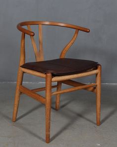 a wooden chair with a leather seat pad on the back and arm rests against a gray wall