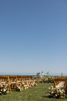 an outdoor ceremony set up with wooden chairs and flowers on the grass by the ocean