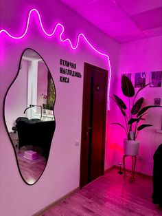 a mirror that is on the side of a wall in a room with pink lighting