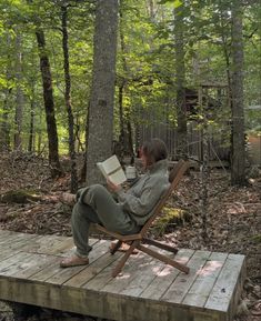 a man sitting in a chair on top of a wooden platform next to trees and holding a book