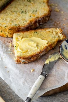 two slices of bread with butter on them next to a small bowl and knife in the foreground