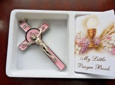 a pink and gold cross in a white box with an open book next to it