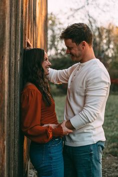 a man and woman standing next to each other in front of a wooden structure smiling