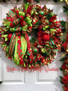 a christmas wreath with green and red bows hanging on a white door, decorated with pine cones