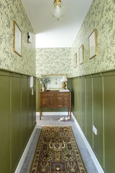 a hallway with green walls and carpeted flooring next to a wooden dresser topped with a mirror