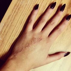 a woman's hand with black nail polish sitting on top of a wooden table