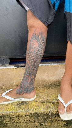 a man with a tattoo on his leg standing next to a door and wearing sandals