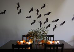 a dining room table with candles and bats on the wall above it, along with pumpkins