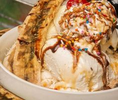 an ice cream sundae with bananas and sprinkles in a white bowl