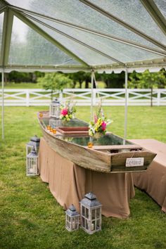 a table with flowers and lanterns on it under a tent in the middle of a field