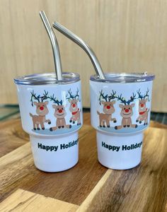 two white cups with reindeer designs on them and the words happy holidays written in black