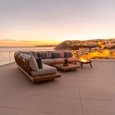 a couch and table sitting on top of a patio next to the ocean at sunset