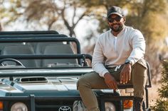 a man sitting on the back of a green truck in front of trees and bushes