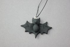 a black bat shaped ornament hanging from a string on a gray surface with two bats attached to it