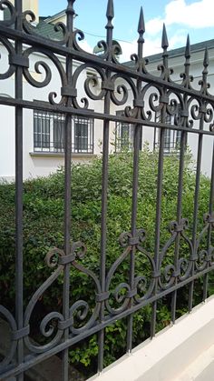 an iron fence is shown in front of a house and bushes on the other side