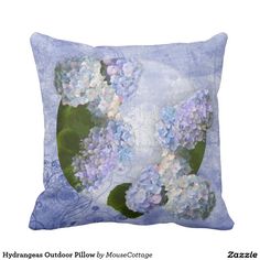 a blue pillow with white and purple flowers on it's side, in front of a white background