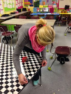 a woman is painting a checkered black and white floor in a classroom with lots of desks